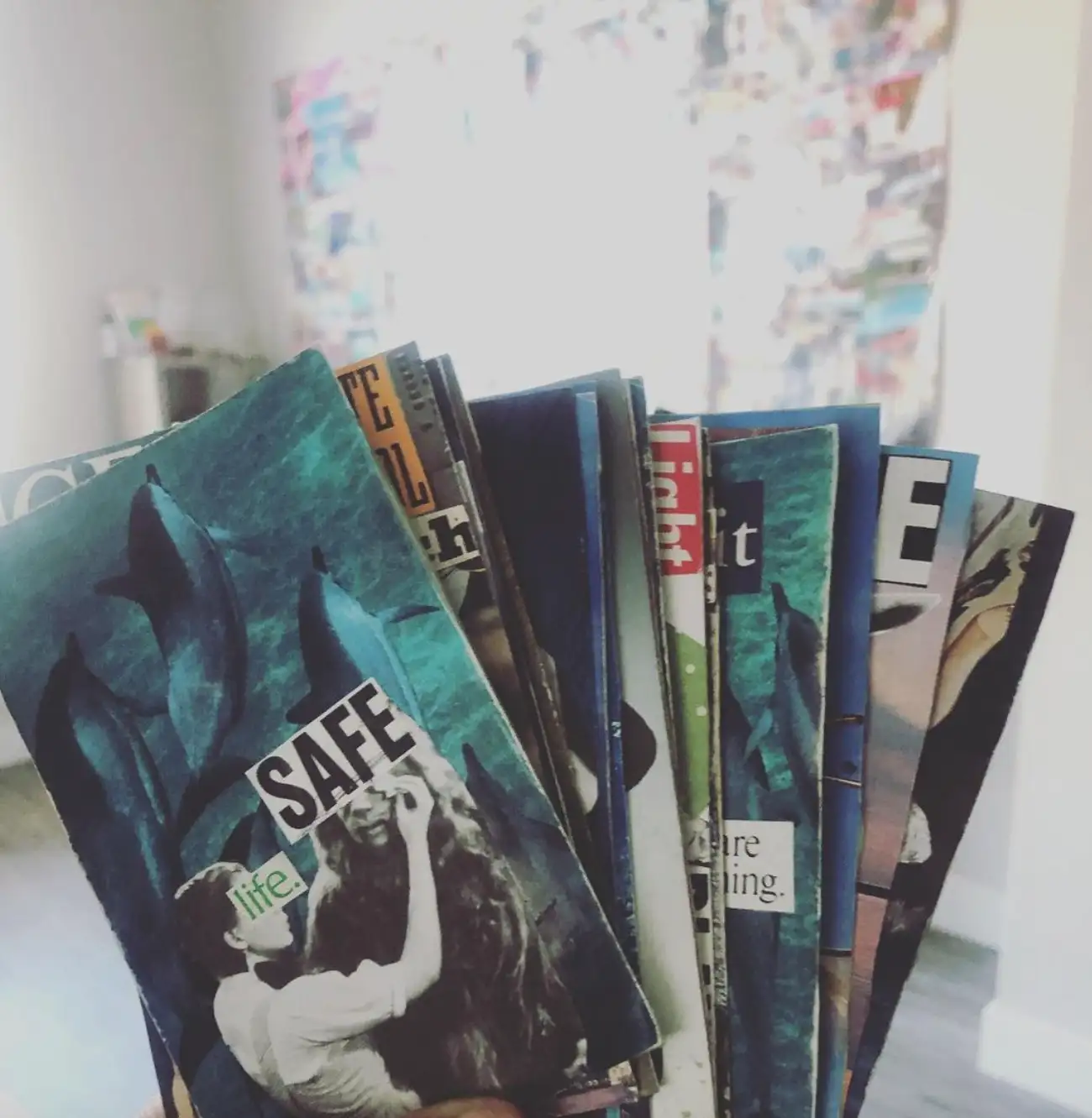 A hand holding a fanned stack of small collage cards; one card reads “Safe.”